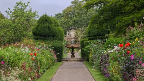 Summer borders with vibrant flowers and a path towards a stone urn at Nymans, West Sussex